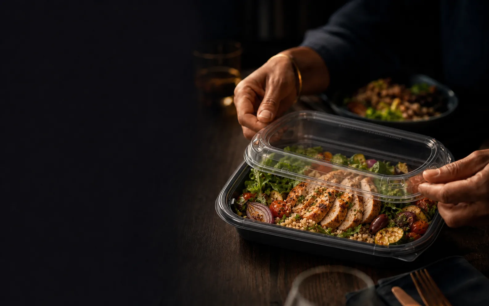 A vibrant prepared meal protected inside a clear food container at a shared table