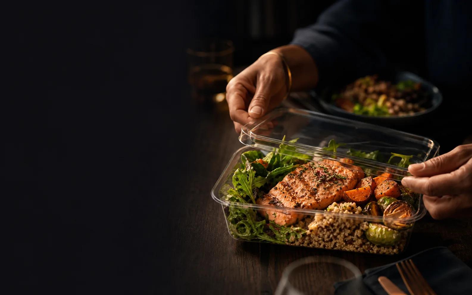A vibrant prepared meal protected inside a clear food container at a shared table